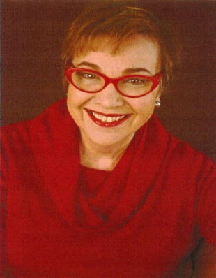 A photograph of author Patricia J. Marino. She is wearing red glasses, a red cowl-neck sweater, and red lipstick. She has short brown hair.