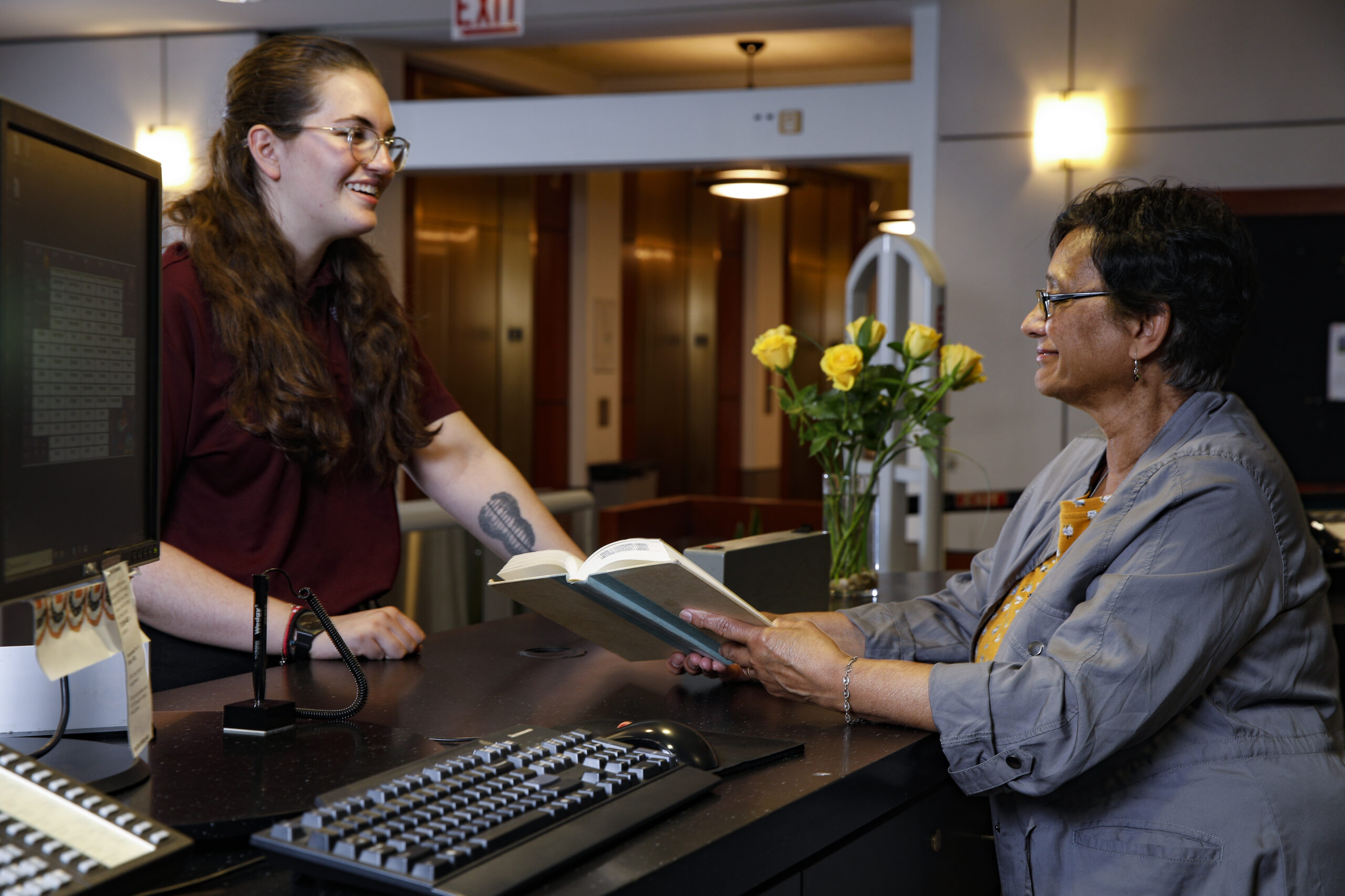 person standing in front of the Circulation Desk while the faculty librarian helps them with checking out a book