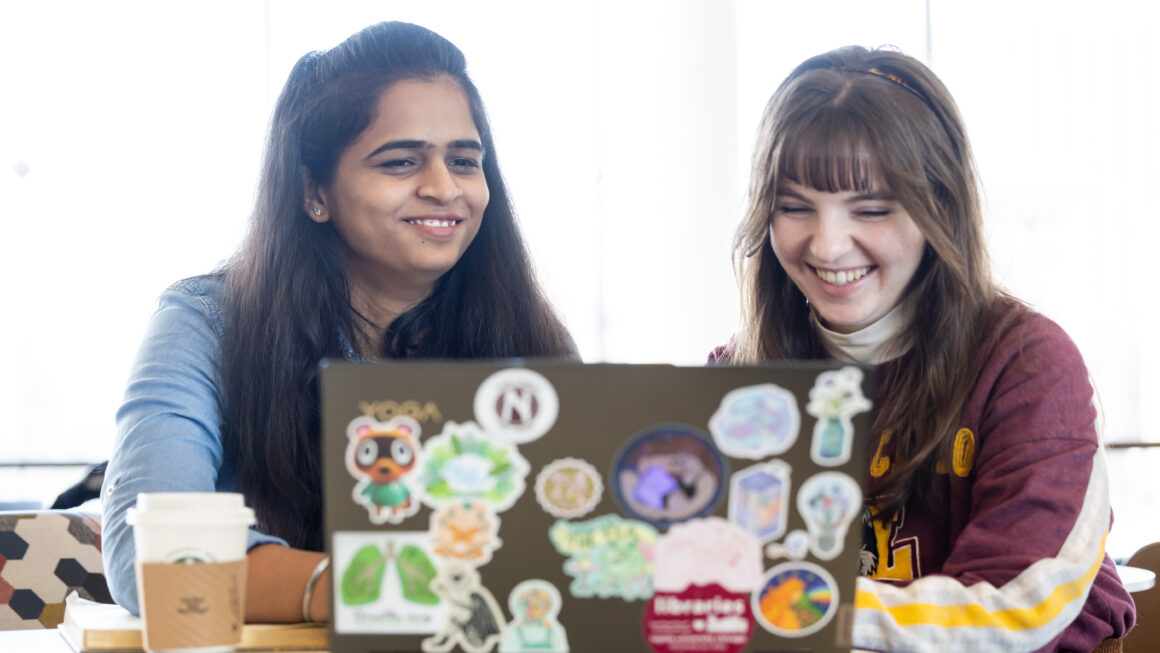 two students sitting next to each other looking at a laptop