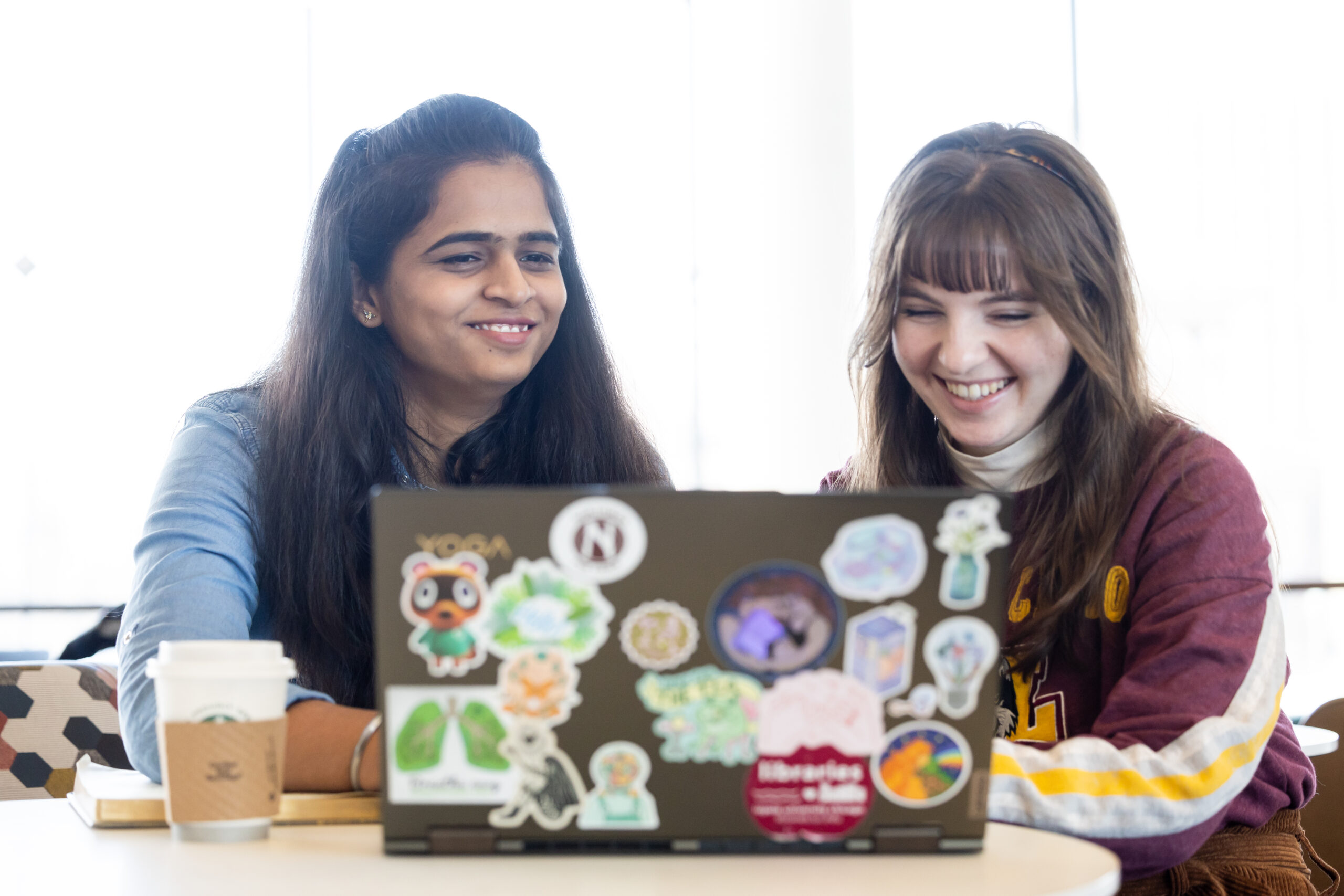 two students sitting next to each other looking at a laptop