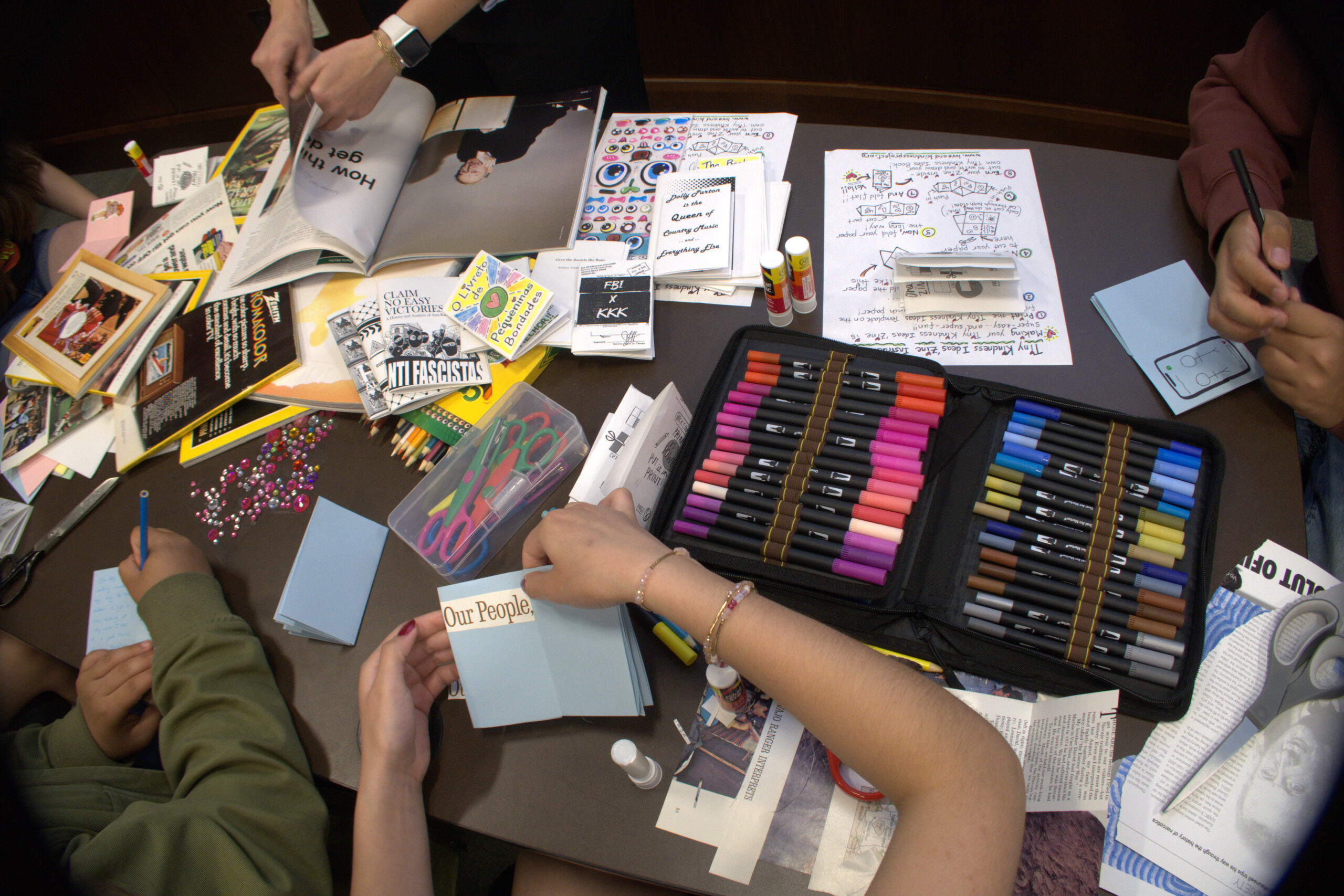 an array of writing and art materials and paper on a table where people are working on an art project