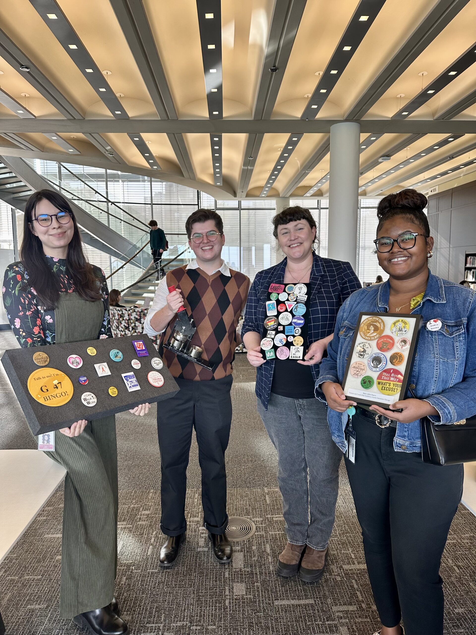 Four people standing holding display boards with various buttons with designs.