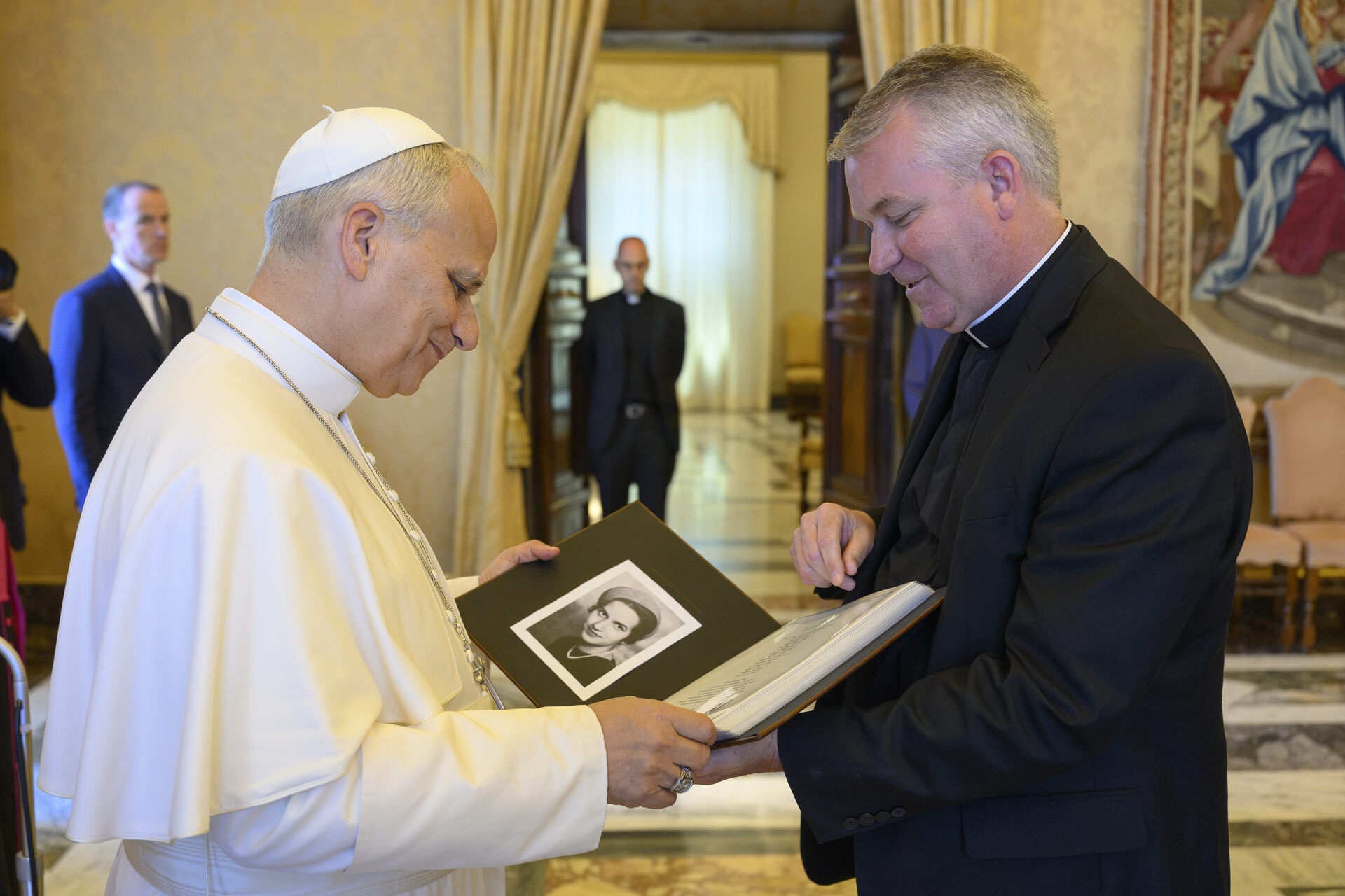 Pope Leo XIV on the left is holding an album showing a black and white photo on the left side. Album is given by the person on the right who is Fr. Tom Neitzke, SJ of Loyola University Chicago.